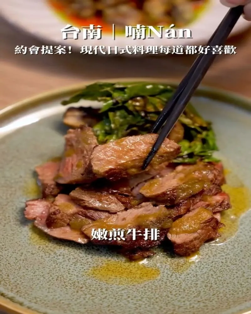 Sliced pan-seared beef steak on a plate with greens, chopsticks lifting a piece; Chinese caption overlaid reads '嫩煎牛排'.